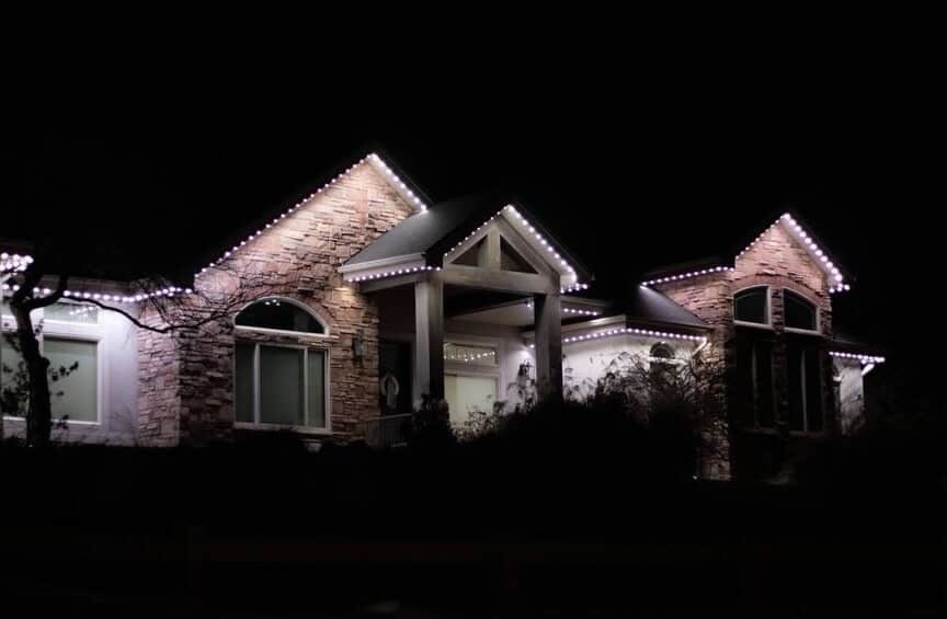 Stone and stucco home outlined in cool white Ember LEDs at dusk